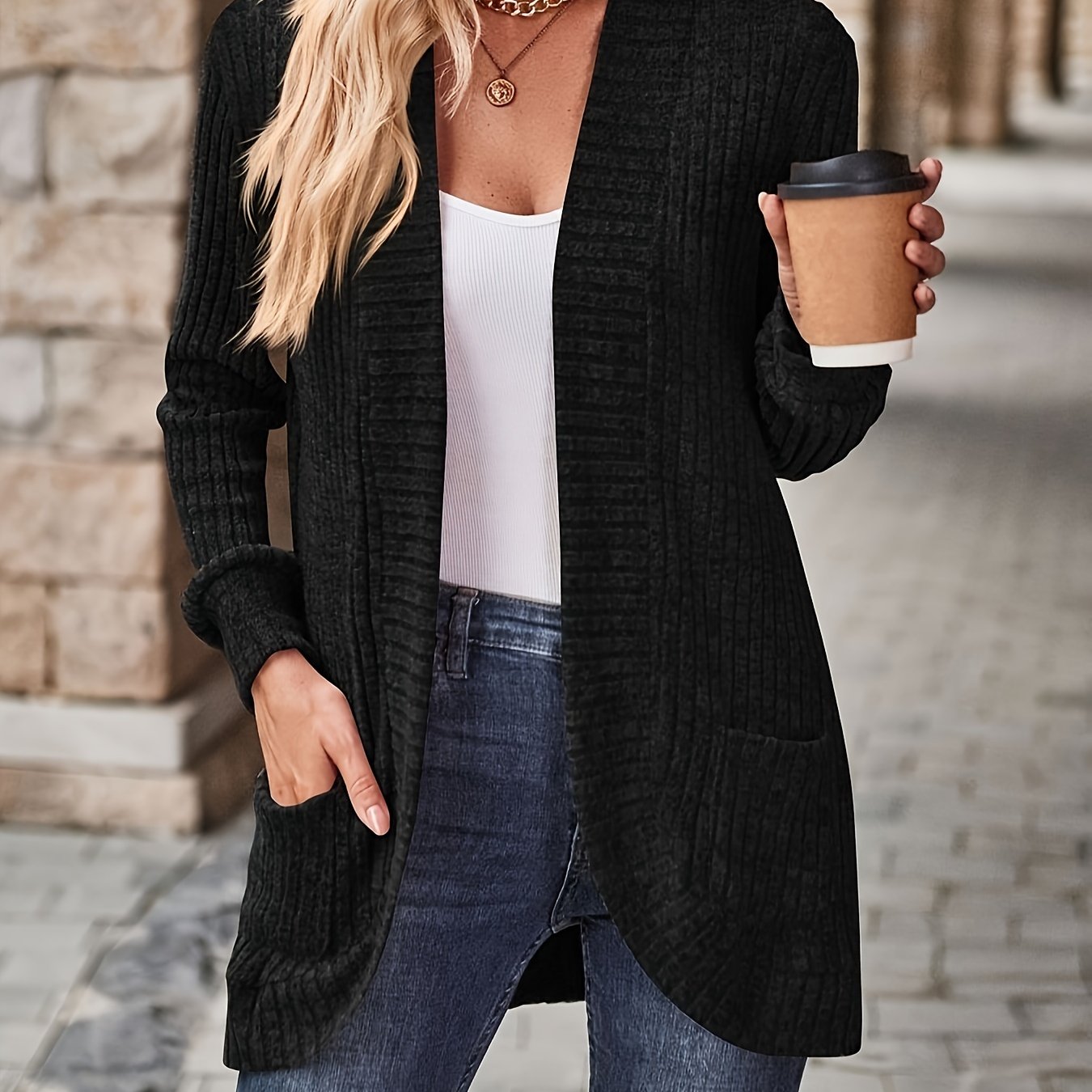 Woman in black cardigan holding coffee cup while walking on brick pathway