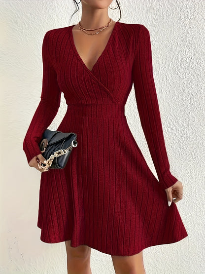 Woman in elegant red ribbed knit dress with long sleeves, holding a black handbag, standing against white textured wall.