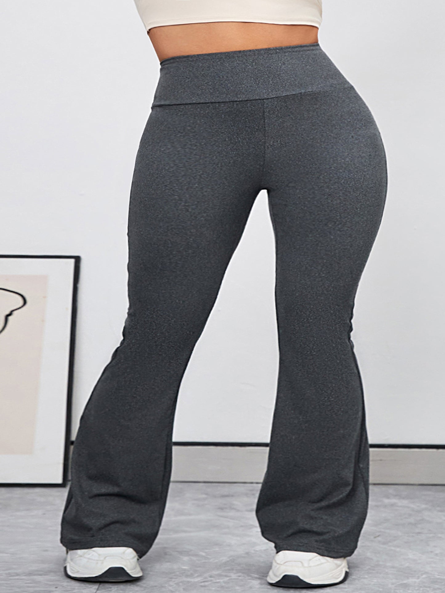 Woman wearing high-waisted, charcoal grey yoga pants with white sneakers, standing in a modern room.