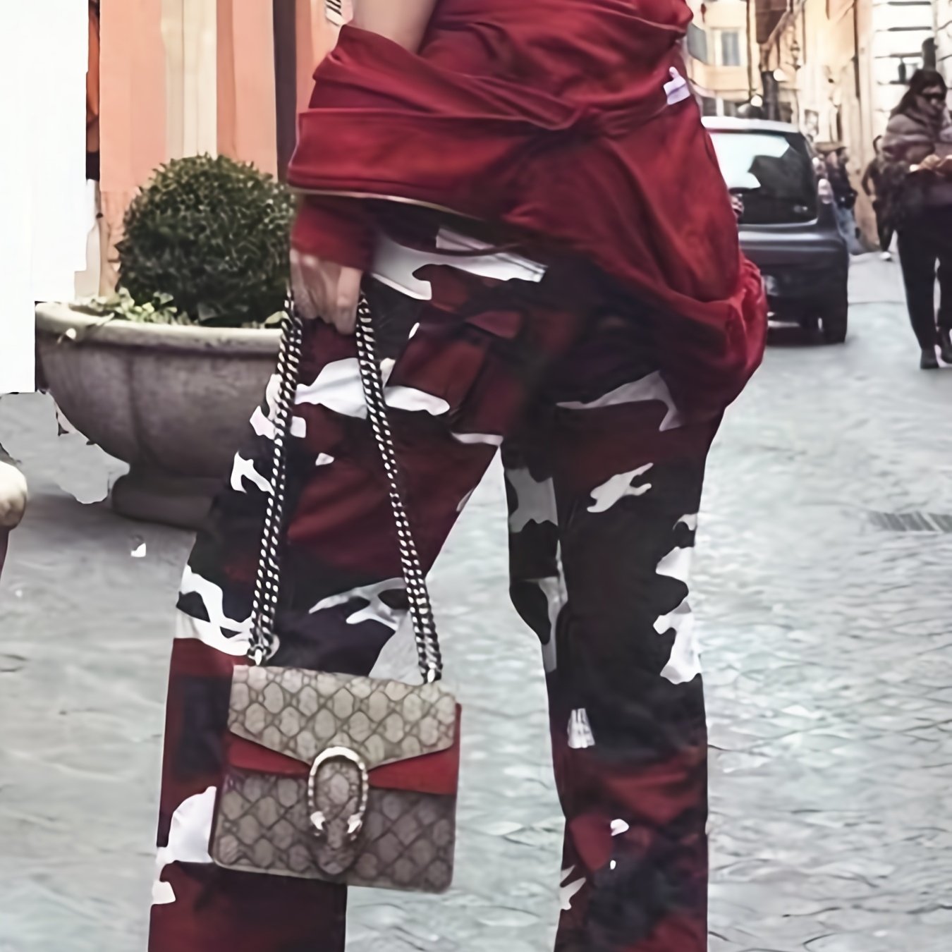 Fashionable streetwear featuring red camouflage pants and a stylish designer handbag in an urban setting.