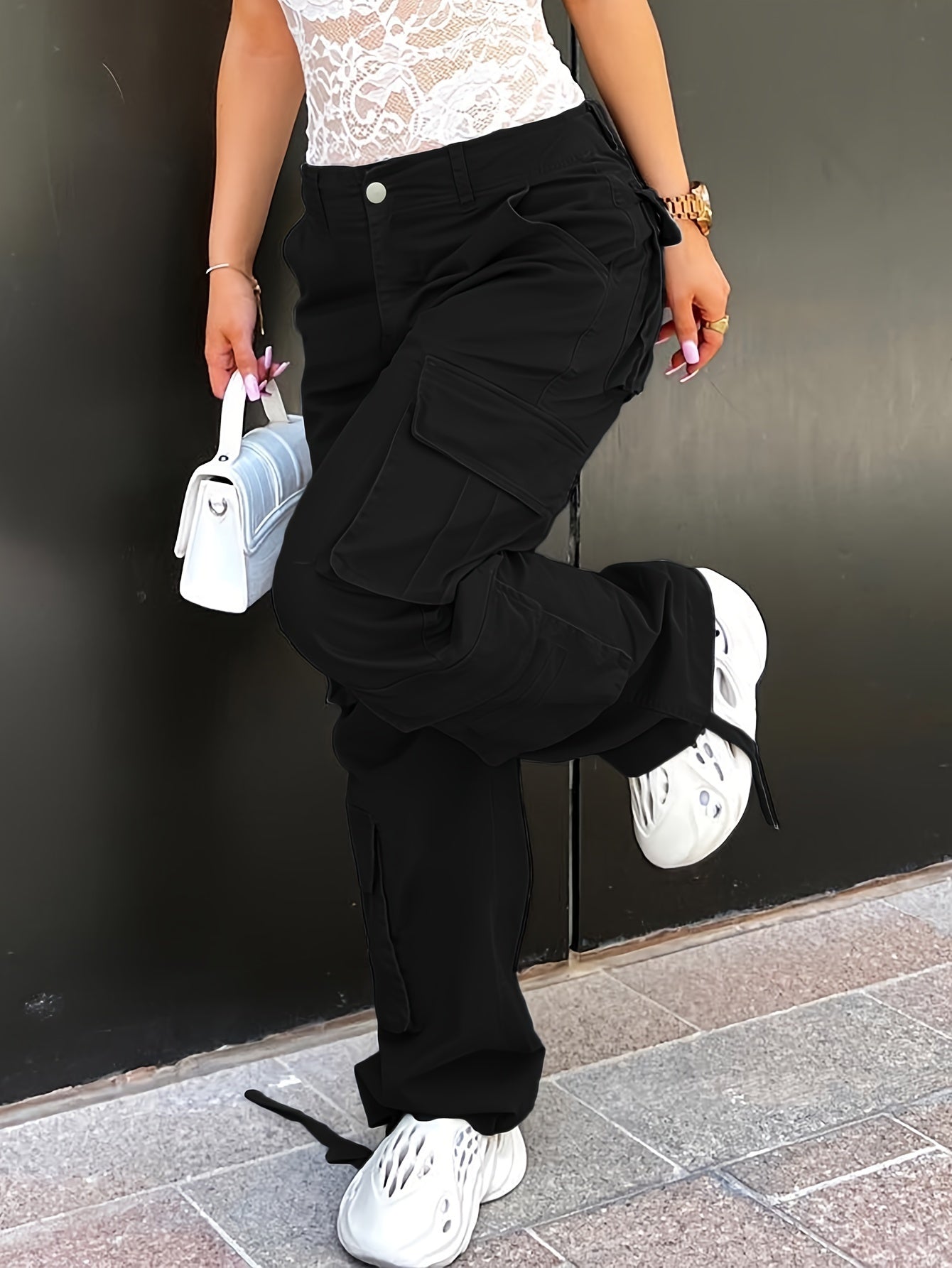 Woman in black plus size Y2K inspired streetwear cargo jeans with side flap pocket and white sneakers holding a small white handbag