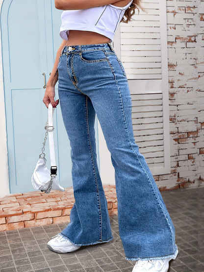 Woman wearing blue high rise flare leg denim pants with raw hem and zipper fly closure, paired with white sneakers and a mini white handbag.