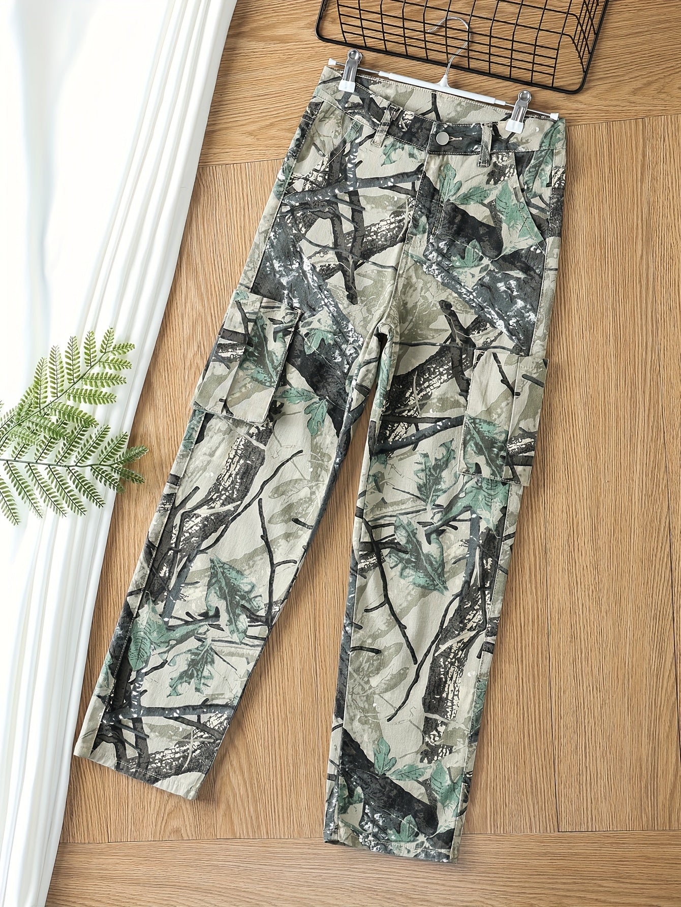 Plus size women's camo print cargo jeans with high stretch, button fly, multiple pockets, and relaxed fit hanging on a hanger.