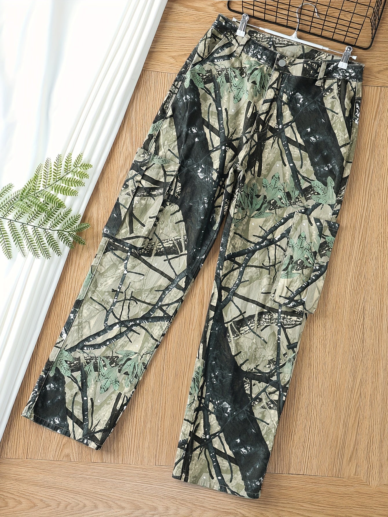 Plus size women's high stretch camo print cargo jeans with multiple pockets, button fly, and relaxed fit on wooden floor with greenery.