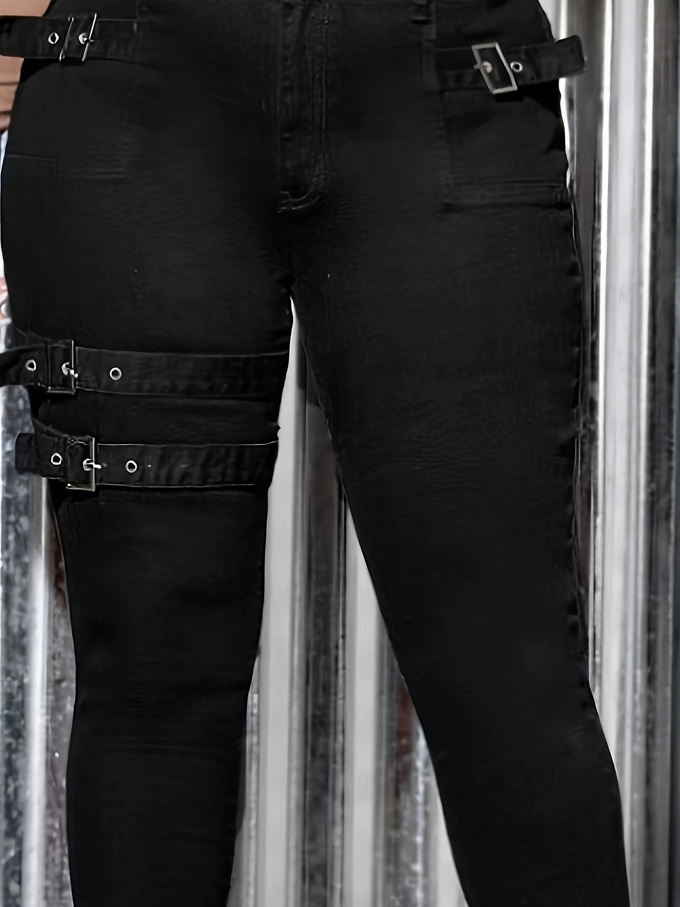 Close-up of black women's plus size skinny jeans with unique strap and buckle design on the legs.