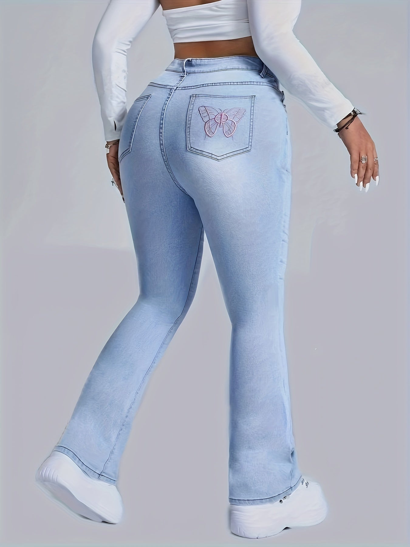 Plus size woman wearing light wash flare jeans with embroidered butterfly design on back pocket, showcasing stretch denim fabric.