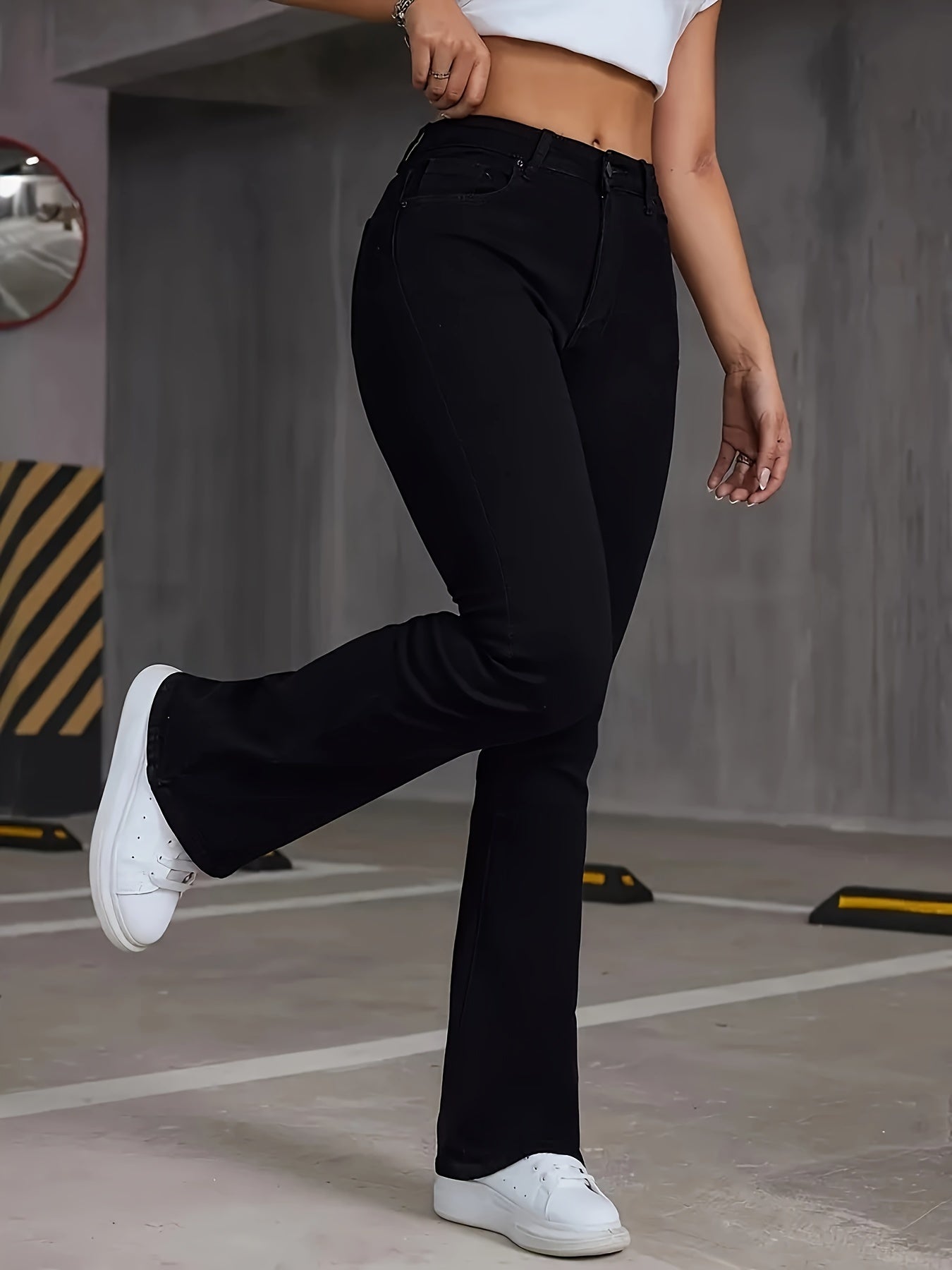 Woman wearing stretchy high-rise bootcut jeans with flare leg in black, paired with white sneakers, demonstrating casual style.