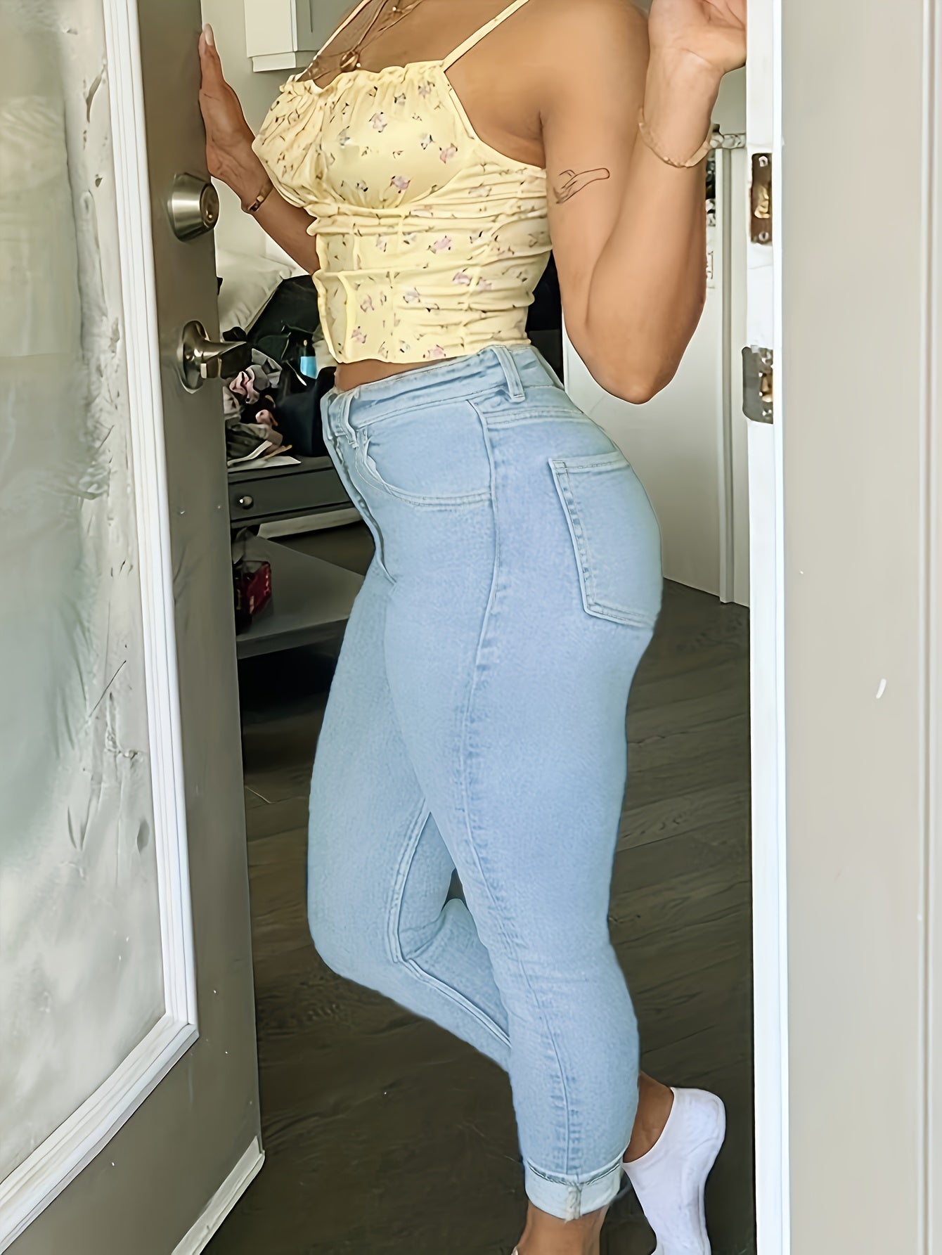 Woman wearing plus-size skinny fit denim pants in washed blue with high waist and zipper closure, pairing with a yellow floral top.